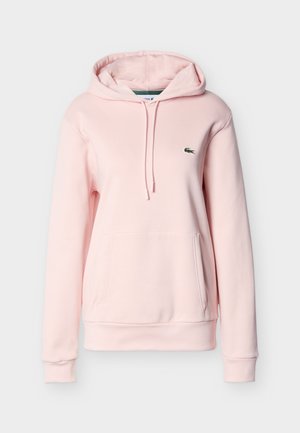 Vaaleanpunainen huppari pehmeästä puuvillamateriaalista. Siinä on kengurutasku, etuosan kiristysnyöri ja pieni vihreä kirjailtu logo rinnassa.