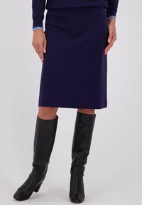 Jupe violette mi-longue en tissu tricoté, texture lisse, associée à des bottes en cuir noires sur le genou avec un design légèrement flou.