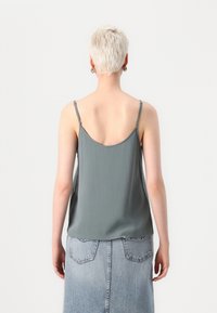 Camiseta de satén gris claro con tirantes ajustables y espalda redondeada. Combinada con una falda de mezclilla de cintura alta con bolsillos traseros.