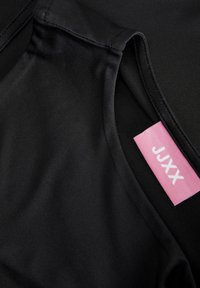 Top in tessuto nero con una texture liscia e lucida; presenta un'etichetta rosa con "JUXX" in carattere bianco lungo il colletto.
