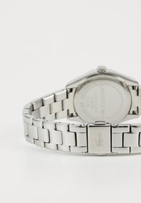 Relógio de aço inoxidável com uma bracelete de metal polido, caixa retangular e logótipo gravado na fivela. Design minimalista com superfícies lisas.