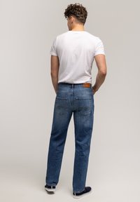 Niebieskie dżinsy o prostym kroju, z subtelnym haftem na tylnej kieszeni i brązową skórzaną łatką na pasku.