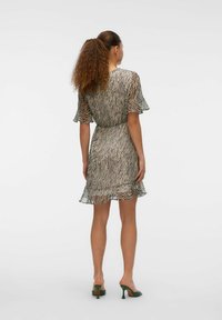 Vestido de estampado de cebra hecho de tela ligera, con mangas de volante, cintura ceñida y un dobladillo fluido. Combinado con sandalias verdes de tacón.