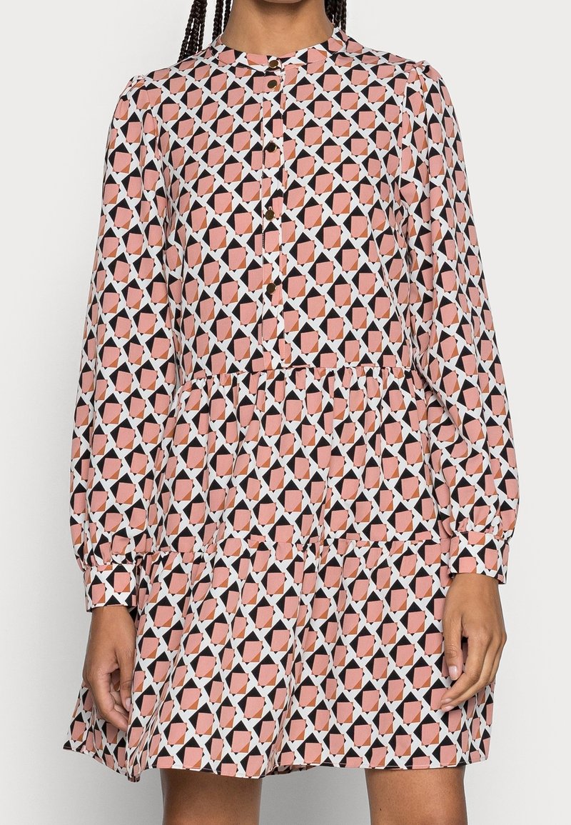 Šaty s dlouhým rukávem zdobené geometrickým vzorem v odstínech růžové, černé a bílé. Šaty mají vrstvený lem a zapínání na knoflíky.