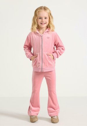 Różowy dres z weluru z kapturem na zamek, ozdobiony serduszkiem, w zestawie z spodniami dzwonami. Miękka faktura i swobodny krój.