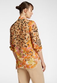 Camicia a maniche lunghe in tessuto leggero, caratterizzata da una combinazione di stampa leopardata e motivi floreali colorati, con maniche arrotolate e orlo curvo.