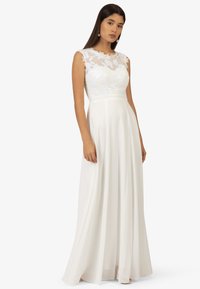 Weißes Kleid mit einem Blüten-Spitzen-Oberteil, ärmellosem Design und einem fließenden Rock. Weiche Stofftextur; knöchellang mit natürlicher Taille.