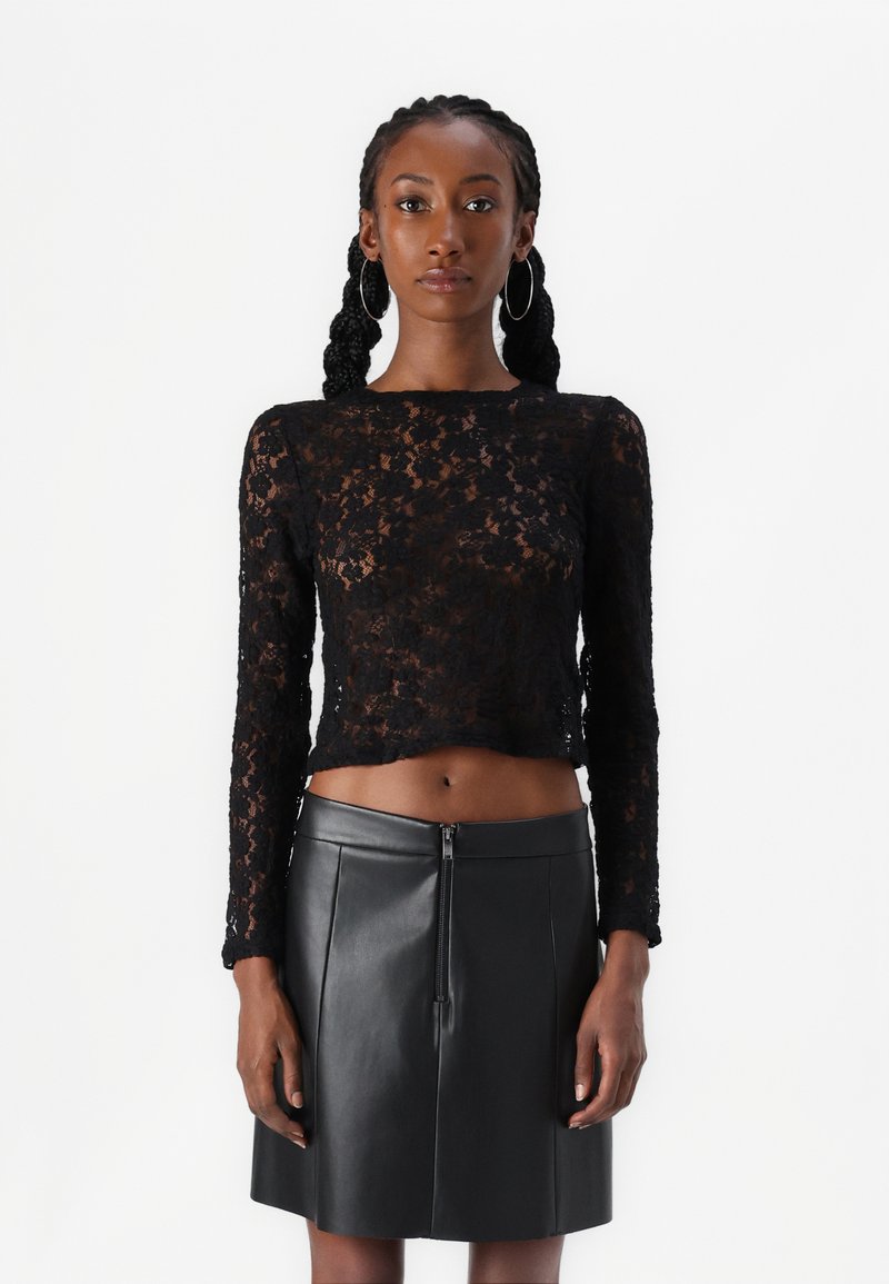 Mustelane pitsäriga must pitsist pikkade varrukatega crop-top, mis on kombineeritud kõrge vöökohaga musta nahkpüksiga, millel on esineed.