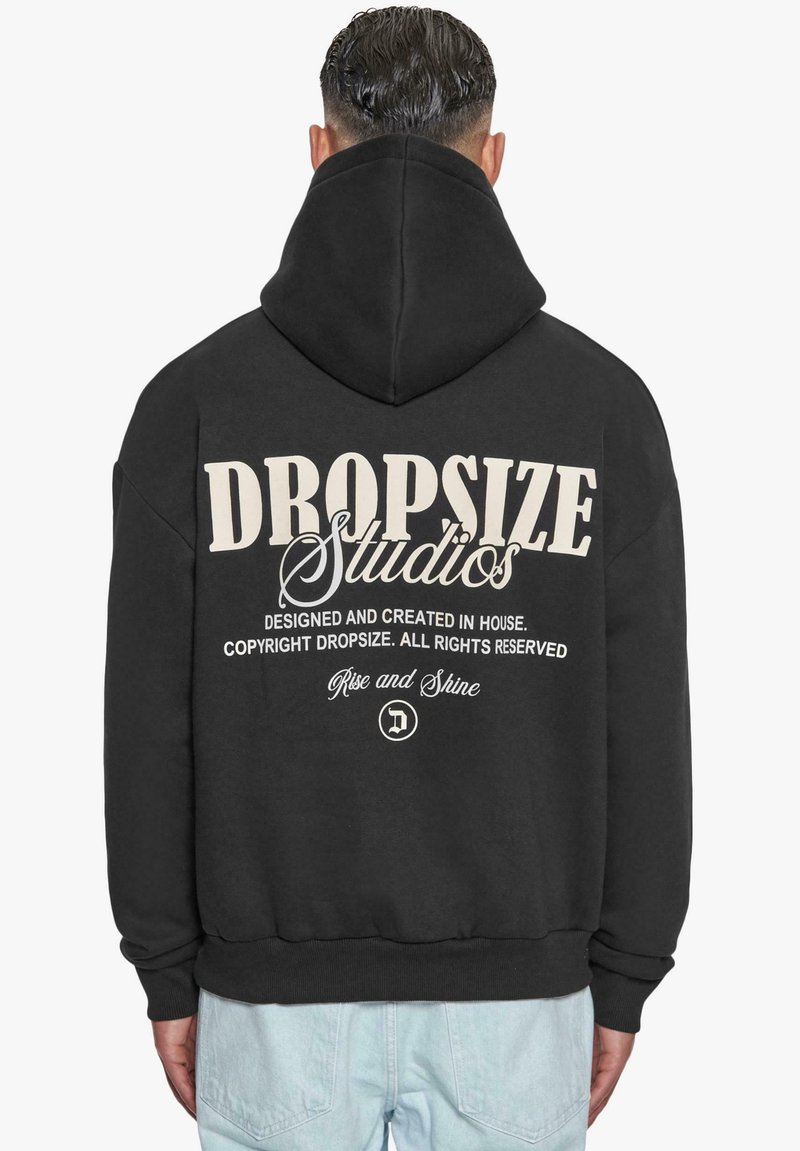 Black hoodie featuring a large white graphic with “DROPSIZE Studios” text on the back, made from soft material with a relaxed fit.