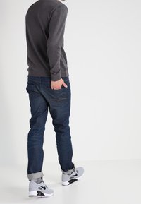 Šedá dlouhá mikina, tmavě modré jeansy s mírným vyblednutím a šedé tenisky. Vyhrnuté manžety a viditelné švy na džínách. Jednoduchý design.