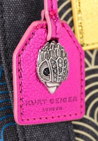 Portachiavi in pelle fucsia con emblema di gioiello argentato e testo in rilievo "Kurt Geiger London" su sfondo di tessuto scuro e decorato.