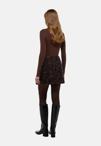 Haut marron à manches longues associé à une mini-jupe brodée de fleurs sombres et des bottes noires à hauteur de genou. Tissu lisse, design ajusté.
