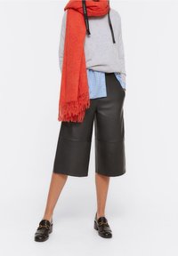Culotte in pelle nera con silhouette a gamba larga, abbinate a una camicia a quadri azzurri e a una sciarpa frangiata rossa. Mocassini neri completano il look.