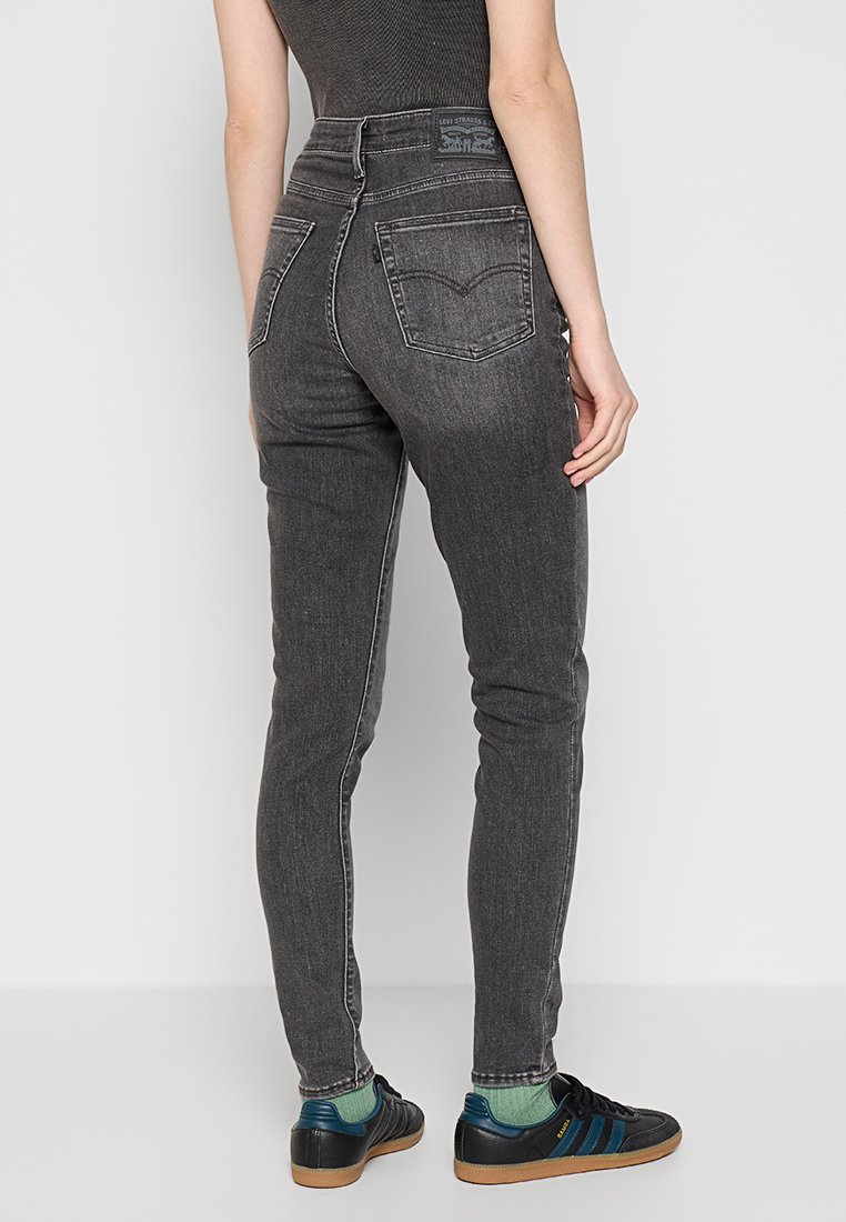 Slim-fit grijze denim jeans met een hoge taille, subtiele vervaging en twee achterzakken. Draagt het met donkere sneakers en groene sokken.