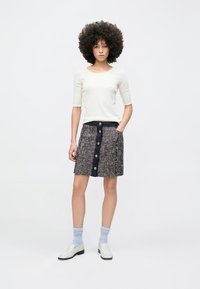 Wollen rok met een mix van texturen, een marineblauwe tailleband, vijf grote knopen aan de voorkant, gecombineerd met een aansluitend crèmekleurig topje en witte schoenen.