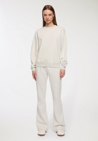 Jasnoszara bluza i dopasowane dzwony wykonane z miękkiego materiału. Góra ma okrągły dekolt i ściągacze, a krój jest luźny.