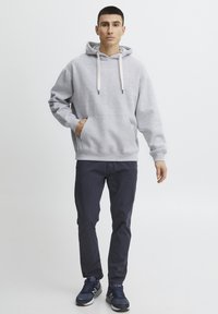 Gray hooded sweatshirt with drawstrings, front pocket, and ribbed hem, paired with navy pants and blue athletic shoes. Simple, casual design.