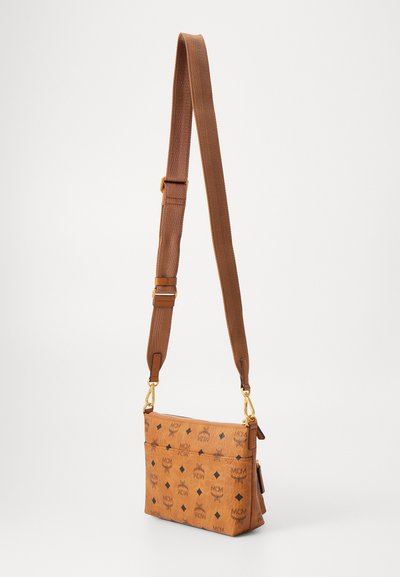 Tan trendig crossbody-väska med mörkt tryckt logotyp, med dragkedjestängning och justerbar rem, prydd med detaljer i guldton.