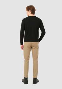 Camicia nera a maniche lunghe abbinata a pantaloni beige, vista da dietro. L'outfit presenta un design semplice e una texture in tessuto morbido.