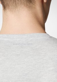Jasnoszary t-shirt z okrągłym dekoltem i widocznym szwem. Etykieta "PROCHNIK" jest subtelnie nadrukowana blisko kołnierzyka z tyłu.