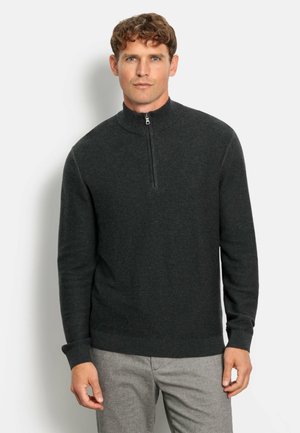 Donkergrijs pull-overtrui met ritssluiting, met ribstructuur, lange mouwen en een aansluitende zoom, gedragen over lichtgrijze broek.