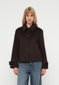 Chaqueta de mezcla de lana marrón con cuello puntiagudo, cinco botones frontales y puños abotonados. Forma desestructurada y textura suave.