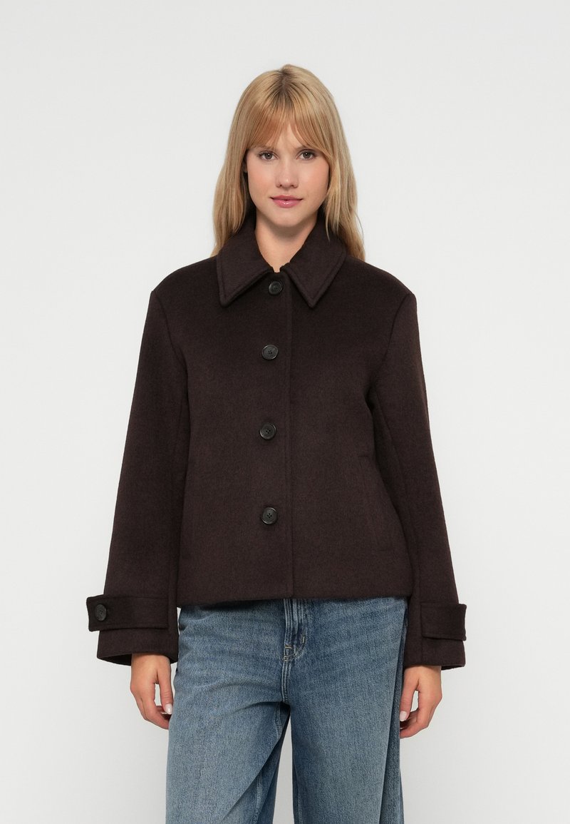 Chaqueta de mezcla de lana marrón con cuello puntiagudo, cinco botones frontales y puños abotonados. Forma desestructurada y textura suave.