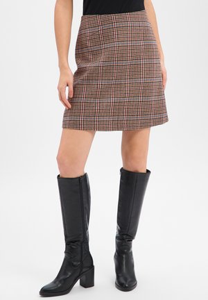 Spódnica w kratę w odcieniach brązu, czerwieni i niebieskiego; krój w kształcie litery A, długość do kolan, teksturowana tkanina. W zestawieniu z czarnymi skórzanymi kozakami za kolano.
