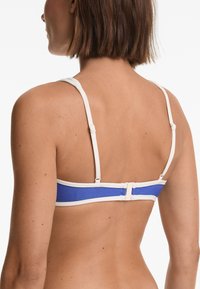 Blå bikiniöverdel med vita remmar, med justerbara spännen och en slät yta. Visar en enkel, funktionell design.
