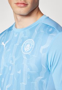 Maillot de football bleu ciel en tissu léger, avec un design texturé, le logo de Manchester City et la marque Puma sur l'épaule.