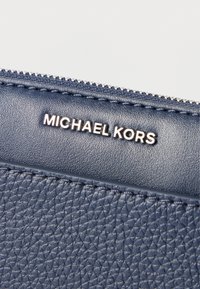 Denim modra usnjena denarnica z zadrgo; teksturirana površina; na sprednji strani srebrna nalepka z napisom "MICHAEL KORS".