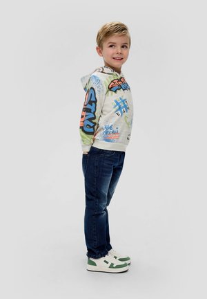 Witte hoodie met kleurrijke graffiti-style print, blauwe jeans en witte sneakers met groene accenten. Casual pasvorm en een soepele textuur.