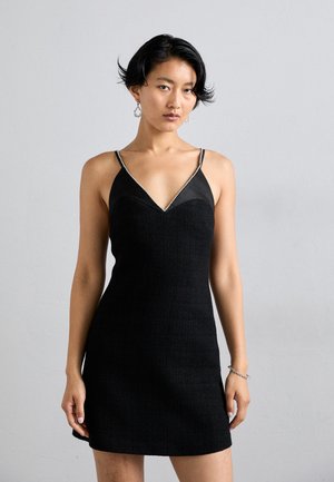 Musta mekko, jossa on tiukka siluetti, V-aukko ja ohuet olkaimet. Päällisen pinta on teksturoitu ja yläosa on sileä.