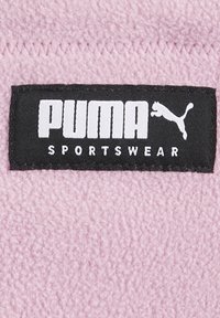 Puma-Sportbekleidungsmarke auf weichem pinkfarbenem Stoff, mit fettem weißen Text und einem schwarzen Hintergrund, sowie einem kleinen Logo eines Pumas.