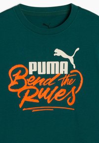 Zielona bawełniana koszulka z okrągłym dekoltem, z wyrazistym pomarańczowym i białym napisem "PUMA Bend the Rules" oraz logo Pumy powyżej.
