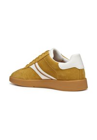Baskets en daim jaune avec des rayures blanches, bout arrondi et accents de talon blancs. Semelle en caoutchouc avec une texture antidérapante.