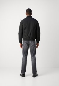 Svart bomberjakke med elastiske mansjetter og hem, kombinert med grå denimjeans. Antrekket har et enkelt, funksjonelt design uten synlige logoer.
