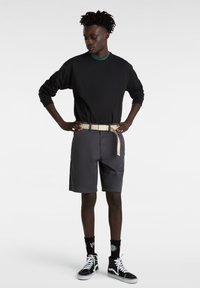 Schwarzes Langarmshirt, graue Shorts, beiger Gürtel, gemusterte Socken und schwarze High-Top-Schuhe. Einfaches Design mit lässiger Passform.