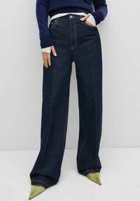 Wijdvallende denim jeans in donkerblauw, met opvallende stiksels, een hoge taille en zijzakken. Gecombineerd met puntige groene hakken.