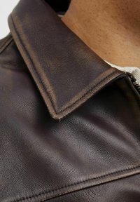 Brown leather jacket featuring a notched collar, smooth texture, subtle sheen, and a zipper detail at the front.