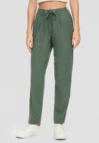 Grüne Leinenmischungshose mit entspannter Passform, gefaltetem Vorderteil, Kordelzugbund und seitlichen Taschen, kombiniert mit weißen Sneakers.