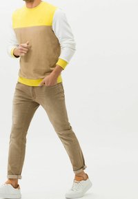 Sudadera de cuello redondo de algodón en amarillo, beige y blanco. Combinada con jeans ajustados de color marrón claro y zapatillas blancas. Detalles de tela texturizada visibles.