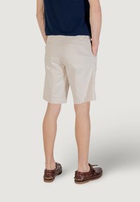 Shorts beige à coupe droite, en coton léger, avec des poches latérales et un dos épuré, associés à des chaussures bateau marron.