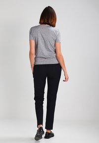 Šedé tričko s krátkými rukávy s jemným vzorem textu, doplněné černými přiléhavými kalhotami a černými plochými botami, pohled zezadu.