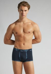 Blaue gemusterte Boxershorts aus weichem Stoff, mit einem kontrastierenden Bund und einer engen Passform, die einen modernen Schnitt und Design aufweisen.