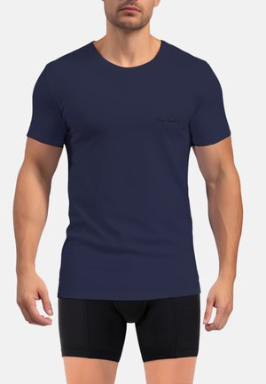 Homme portant un t-shirt bleu marine ajusté à manches courtes et un boxer noir, debout devant un fond uni.