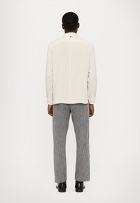 White long-sleeve shirt with vertical stripes and a pointed collar, paired with gray textured trousers and black shoes.