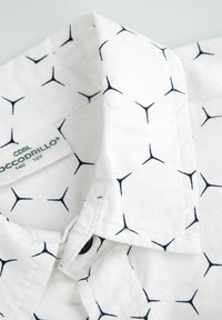 Biała koszula z guzikami z czarnym, geometricznym wzorem. Posiada klasyczny kołnierzyk, zapięcie na guziki oraz miękki materiał o lekkiej teksturze.