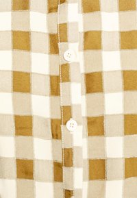 Camisa de botão com padrão quadriculado em bege e castanho claro, com uma textura suave e quatro botões redondos ao longo da pala.