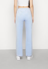 Ljusblå, vida byxor i mjukt tyg med elastisk midja. Har en slät yta och avslutad fåll, parat med vita skor.